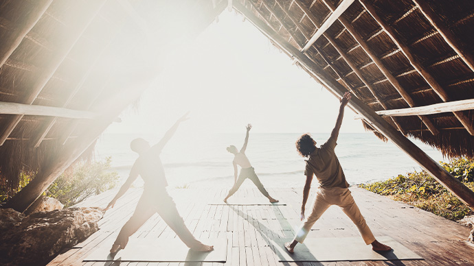 Wide shot of couple taking sunrise yoga class in beachfront pavilion at luxury tropical resort