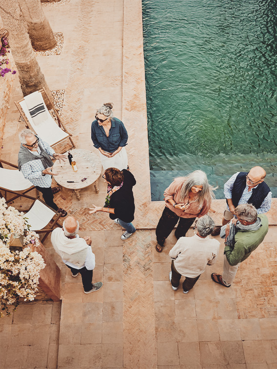 Wide shot overhead view of senior couples in discussion while relaxing at poolside cocktail party at tropical villa